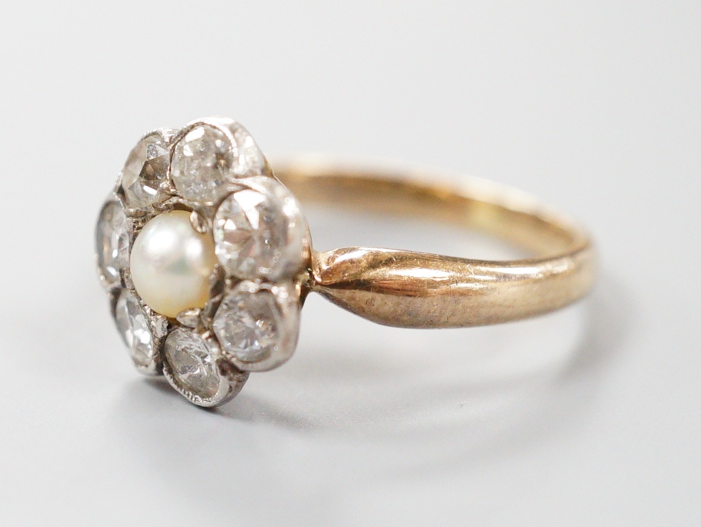 A late Victorian yellow metal, single stone split pearl and seven stone diamond set circular cluster ring, size I, gross weight 3 grams.